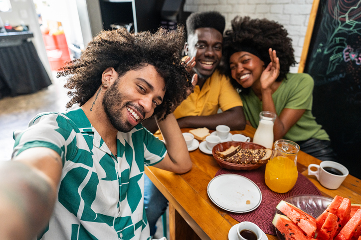 Friends taking selfies while having breakfast at a hostel