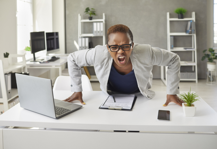 Angry crazy stressed black businesswoman leaning on her office desk and shouting