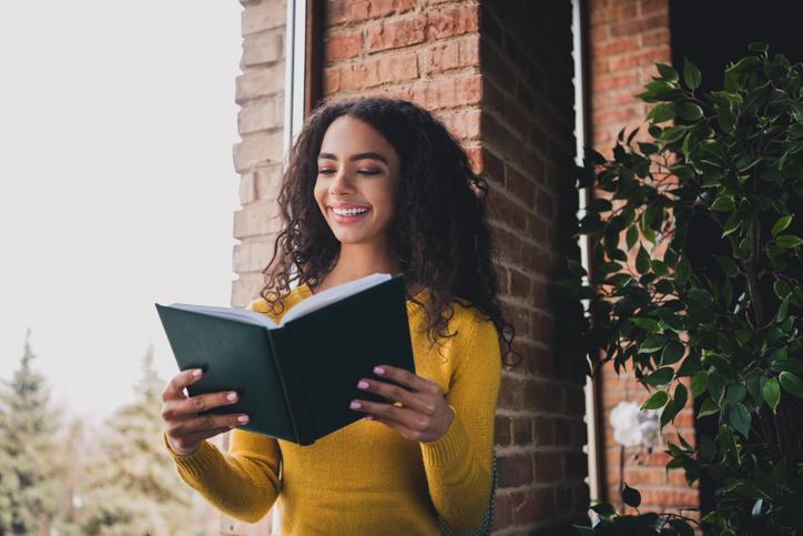 Young woman enjoying a good book indoors by a brick wall in natural light setting