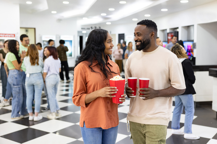 Couple at the cinema holding popcorn and drinks and smiling