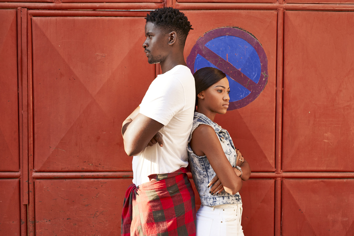 Sulking couple standing back to back in front of red gate