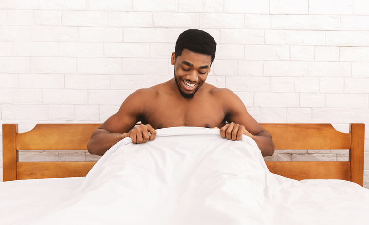Excited african-american man looking at his body part under sheets