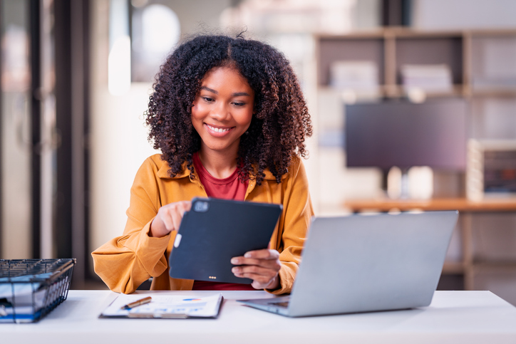 Young African American accountant, financial expert sits in office at desk and works on laptop and documents, checklist and accounting.