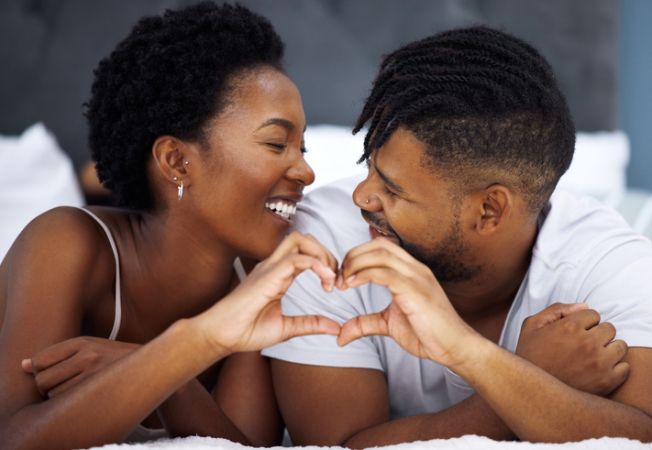 Shot of a young couple making a heart shaped gesture in bed at home