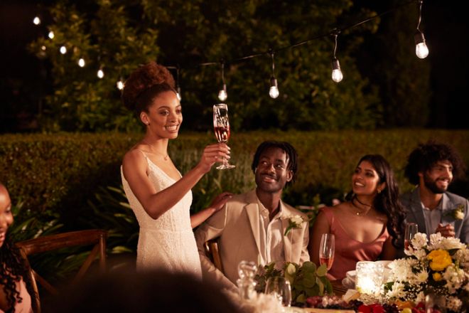 Happy young bride toasting drink while giving speech