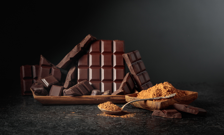 Broken dark chocolate bar and cocoa powder on a black background.