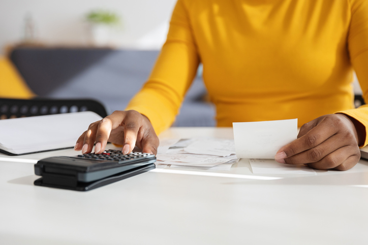 Young adult black woman calculating domestic bills at home using calculator