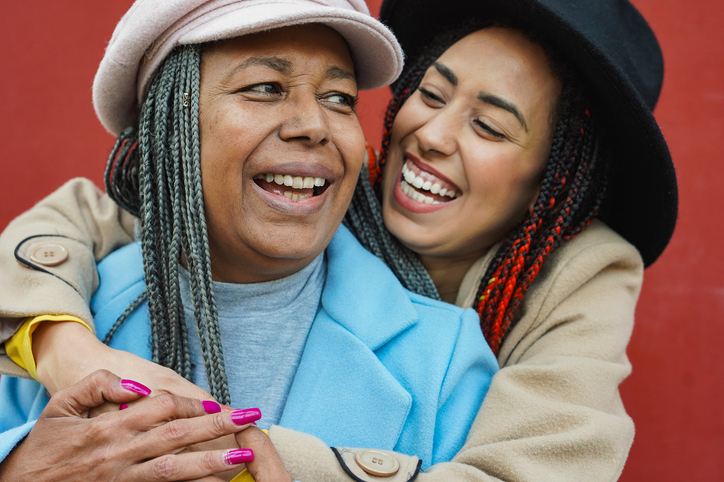 Happy african mother and daughter hugging eacht other in the city during winter travel vacation - Family love and holiday concept - Focus on senior woman face
