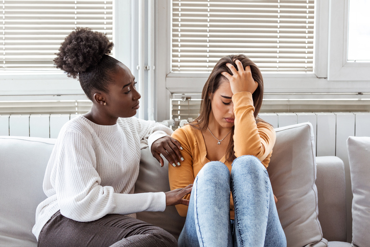 Sad girl and supporting friends trying to solve a problem. Two sad diverse women talking at home. Female friends supporting each other. Problems, friendship and care concept