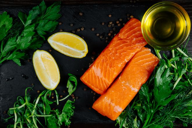 Close-up of fresh salmon pieces with aromatic herbs, lemon and butter.