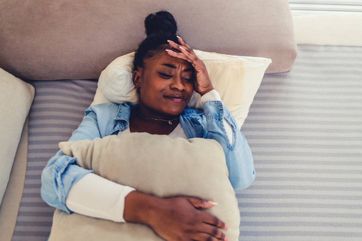 Cropped short of a woman holding a bridge pillow against her stomach on the sofa at home. Photo of a young woman having stomach pain while lying on the couch at home.