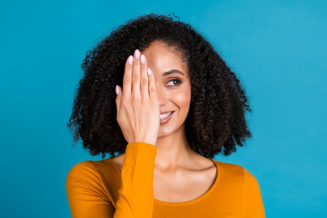 Photo portrait of pretty young girl palm cover half face look empty space wear trendy orange outfit isolated on blue color background