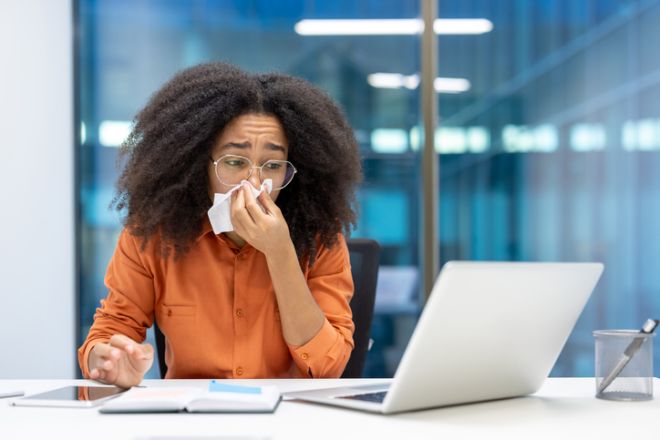 Young professional sneezing while working at her desk in office