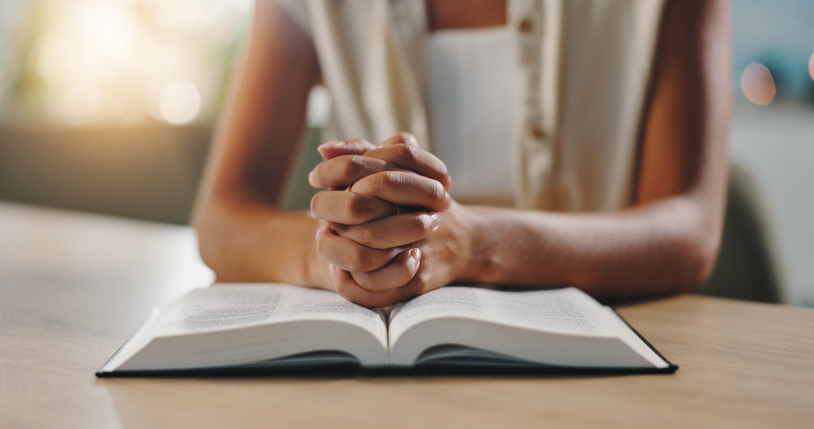 Hands, praying and bible in home with religion, study and hope for change, spiritual or reflection in morning. Person, book and scripture with prayer, worship or learning for Christian faith in house