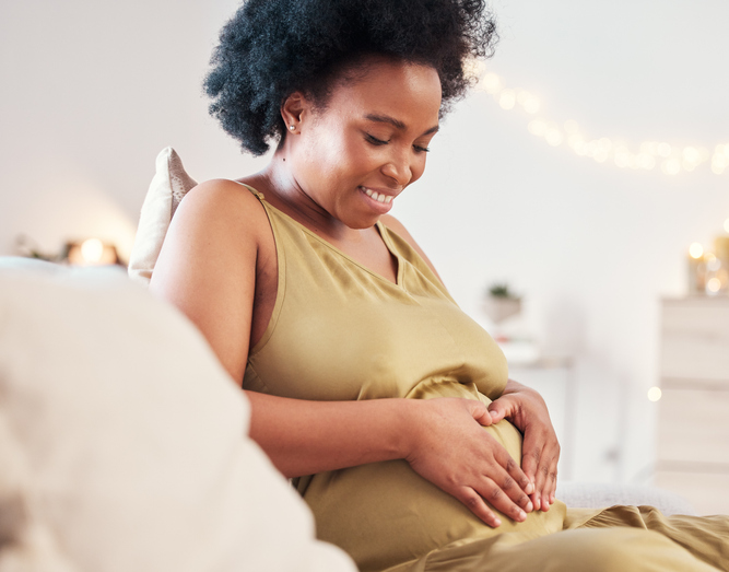 Pregnant stomach, heart hand sign and happy black woman feeling mother hope and love. Mom care, sofa and living room lounge with a person holding abdomen happy about pregnancy and baby in a house