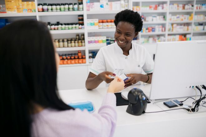 Smiling pharmacist receiving credit card from customer at checkout counter