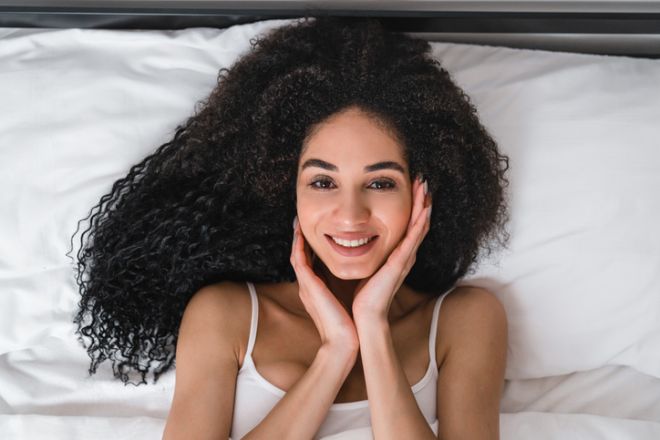 Beautiful african woman lady in white pajamas looking at the camera lying in the bed