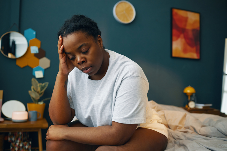 Woman Sitting in Bedroom Holding Head with Hand