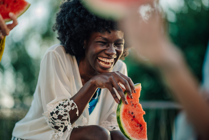 Young woman laughing while eating watermelon slice at a summer party