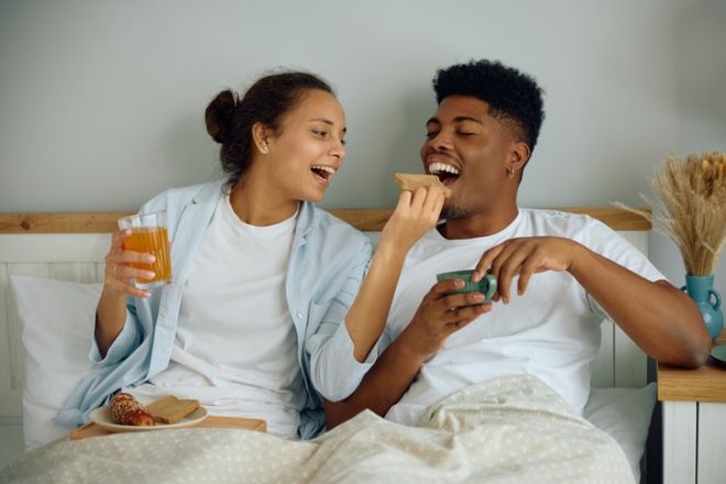 Young multiracial couple having fun while eating breakfast in bed.