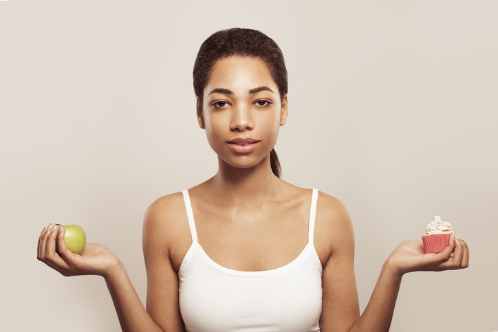 Dieting concept. Young woman choosing between fruits and sweets