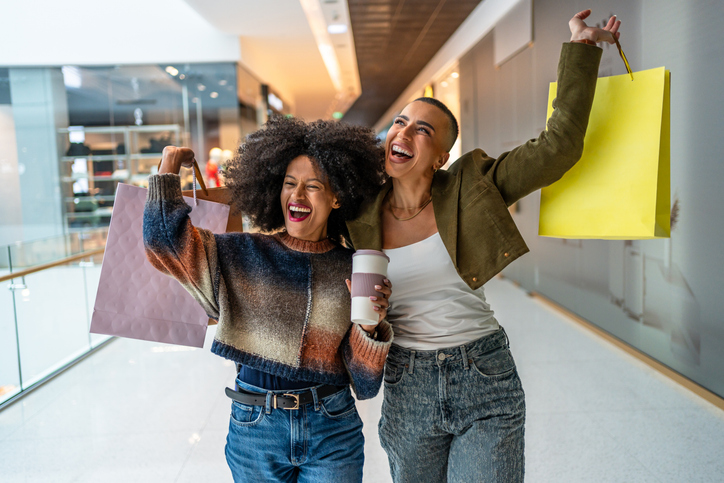 Two young women holding shopping bags and coffee cup, enjoying shopping spree