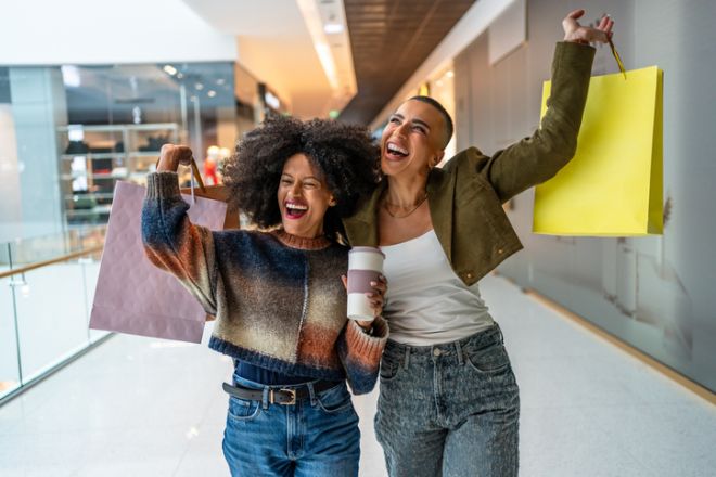 Two young women holding shopping bags and coffee cup, enjoying shopping spree