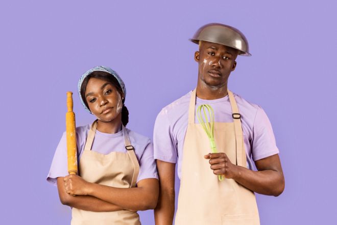 Exhausted black couple with kitchen utensils having hard time baking on color background