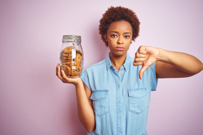 African american woman holding jar of chocolate chips cookies over pink isolated background with angry face, negative sign showing dislike with thumbs down, rejection concept
