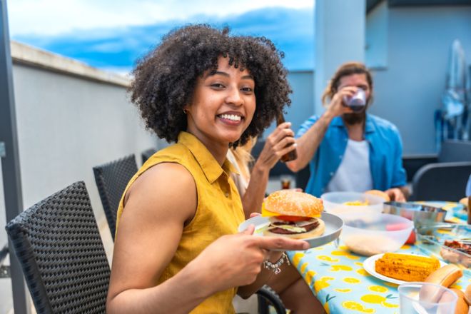 Woman holding burger while enjoying rooftop barbecue with friends