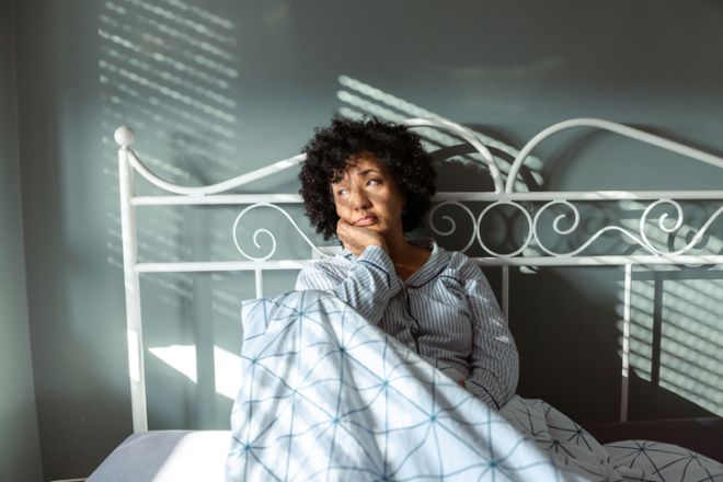 Mature woman in striped pajamas feeling stressed while sitting on the bed in morning light