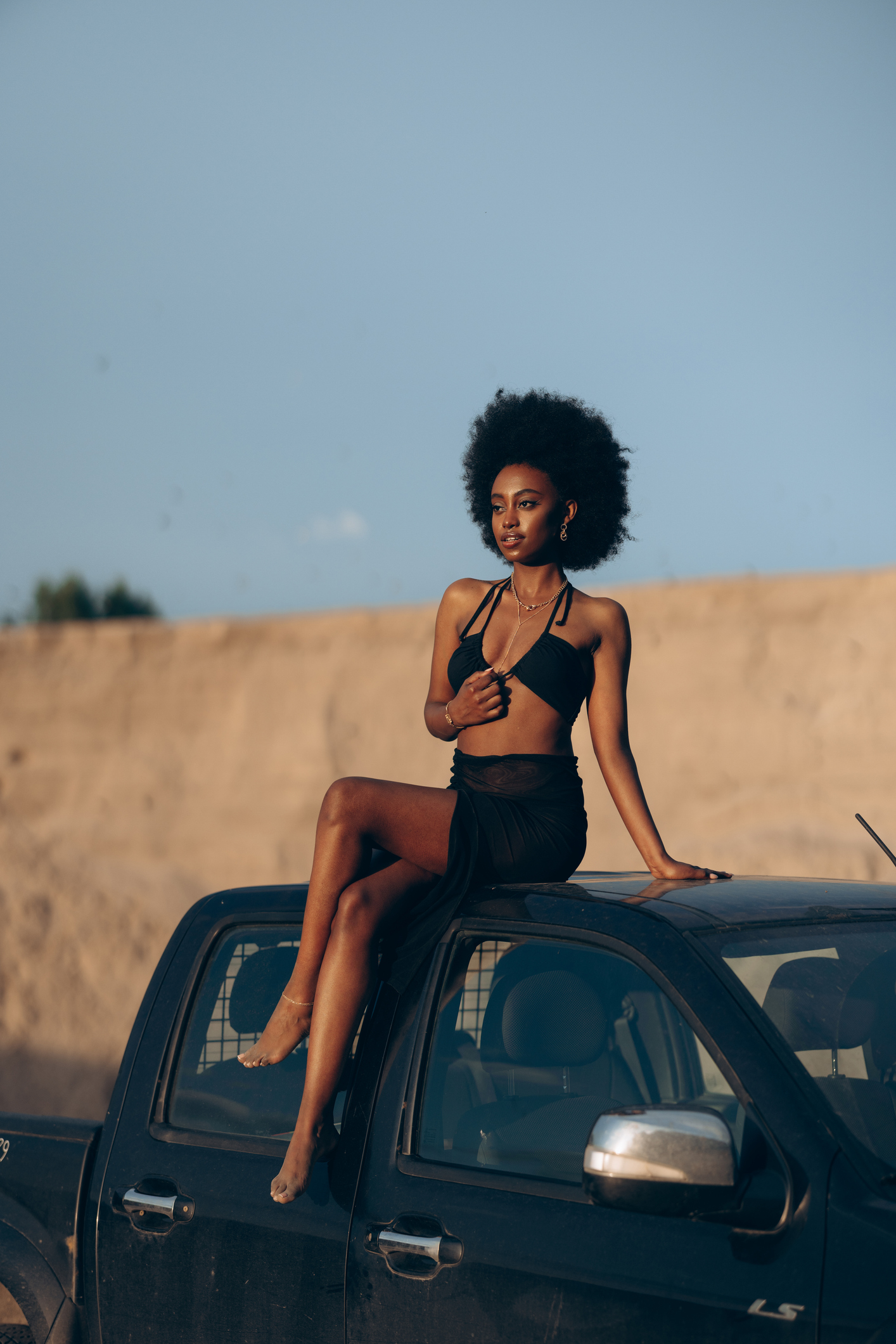Young african woman sitting on top of a pickup truck against background of sandy canyon and sky.