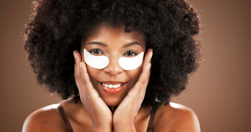 Eye mask, beauty and portrait of black woman in studio for dark circles, hydration and wellness. Dermatology, happy and African person with pads for collagen, anti aging or health on brown background