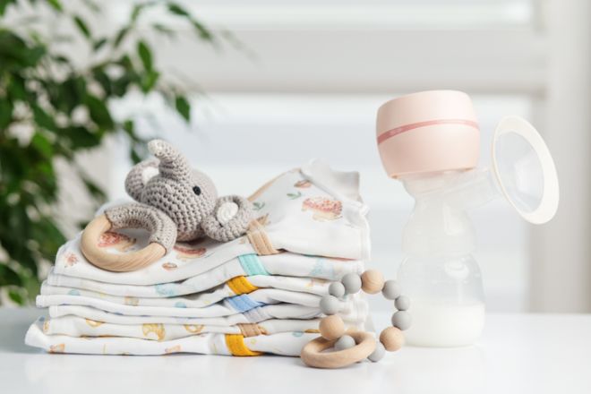 Breast pump with baby clothes and toys on table. Baby care.