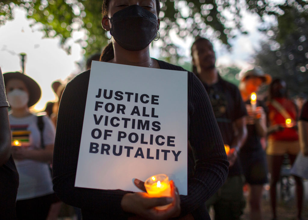 A demonstrator holding a candle and a sign with Justice For...