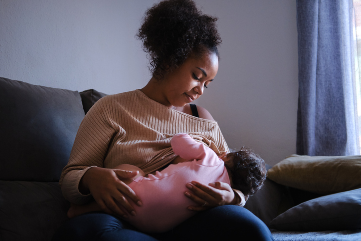 front view portrait of a serene Black woman breastfeeding her little baby in the living room during a regular day. concept family and motherhood