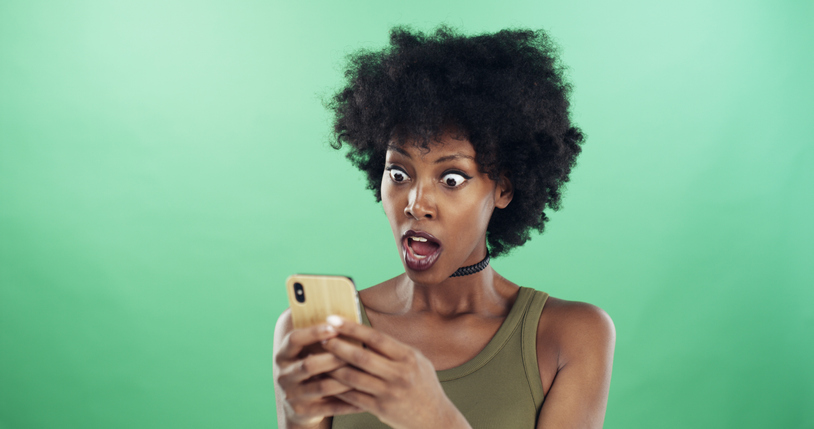 Phone, shock and text message with black woman in studio for communication of bad news or update. App, serious and social media with reaction of angry person on green background for notification