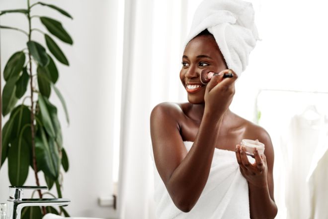 Woman applying skincare routine while smiling in a bright, fresh bathroom with white decor