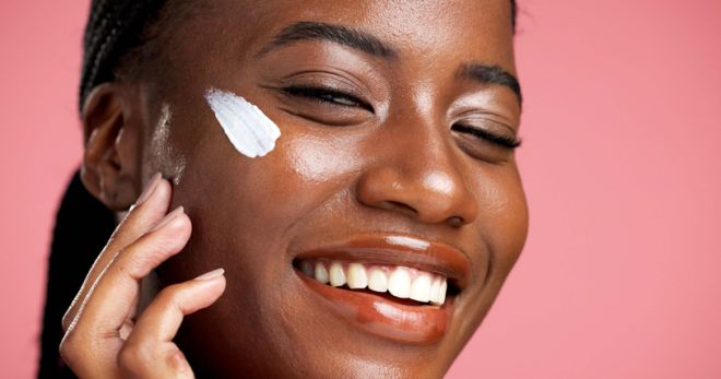 Face cream, happy and black woman in portrait for sunscreen, beauty and facial treatment. Glow, apply and African person in studio with moisturizer, lotion and smile for skincare on pink background