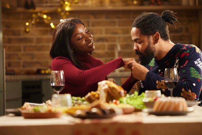Loving black man kissing his wives' hand during Christmas lunch at dining table.