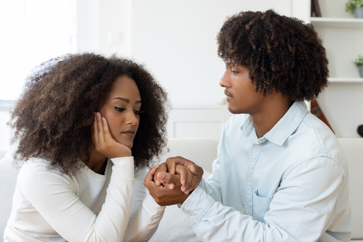 Upset couple sitting on couch and holding hands