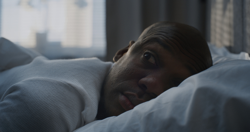 Man Slowly Waking Up in Bed, Resting Head on White Pillow, in Soft Morning Light